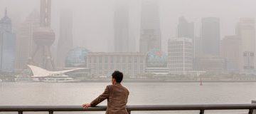 Shanghai, China - April 20, 2010: Air Pollution, high-rises shrouded in heavy smog,  air in City remained severely polluted, man standing on the Bund, and looks at the Pudong District.