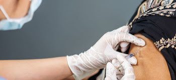 doctor in gloves holding syringe and making injection to senior patient in medical mask