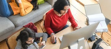 woman working at home in living room, daughters doing home work and hanging around