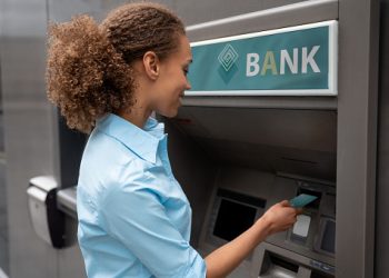 Portrait of an African American woman withdrawing money at an ATM and looking happy - financial concepts. **DESIGN ON BANK AND CREDIT CARD WERE MADE FROM SCRATCH BY US**