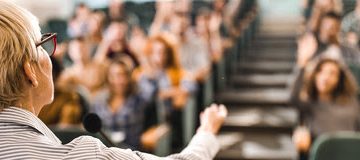 Back view of a senior professor talking on a class to large group of students.