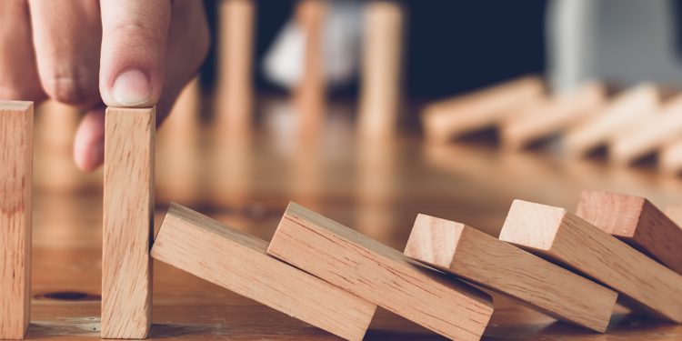 Close up finger businessman stopping wooden block from falling in the line of domino with risk concept.