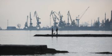 A couple walks a dog on a pier at a coast of the Sea of Azov in Ukraine's industrial port city of Mariupol on February 23, 2022. - Mariupol lies on the edge of the front line separating government-controlled territory from that overseen by Russian-backed separatists in the rebel stronghold Donetsk. (Photo by Aleksey Filippov / AFP)