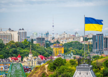 Kyiv, Ukraine cityscape of Kiev and Ukrainian flag waving in the wind during summer in Podil district and colorful new buildings