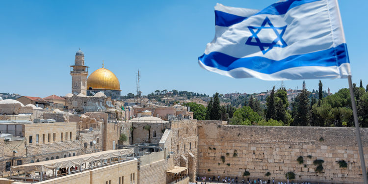 An Israeli flag blows in the wind from an elevated view of the Western Wall. Jewish orthodox believers read the Torah and pray facing the Western Wall, also known as Wailing Wall or Kotel in Old City in Jerusalem, Israel. It is small segment of the structure which originally composed the western retaining wall of the Second Jewish Temple atop the hill known as the Temple Mount to Jews and Christians.