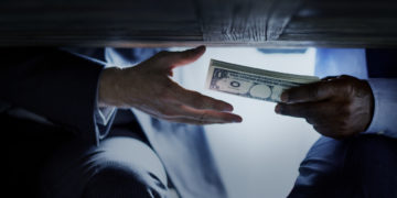 Hands passing money under table corruption bribery