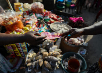 A customer pays with a Ghana cedi banknote at a food market in Accra, Republic of Ghana, on Wednesday, Nov. 3, 2021. Ghana’s inflation rate breached the central bank’s target band in September after supply bottlenecks, a weak cedi and surging energy costs propelled food-price growth to a seven-month high. Photographer: Nipah Denis/Bloomberg