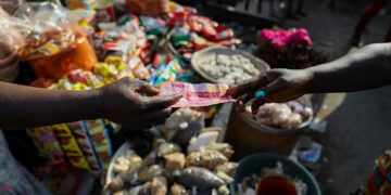 A customer pays with a Ghana cedi banknote at a food market in Accra, Republic of Ghana, on Wednesday, Nov. 3, 2021. Ghana’s inflation rate breached the central bank’s target band in September after supply bottlenecks, a weak cedi and surging energy costs propelled food-price growth to a seven-month high. Photographer: Nipah Denis/Bloomberg