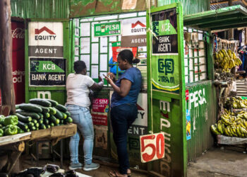 Customers use M-pesa services at a kiosk in Toi Market, an open air market and favorite spot to pick up second hand home goods, clothes, shoes, or just fresh fruit and vegetables in Nairobi, Kenya.