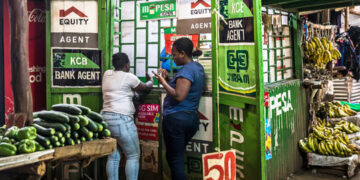 Customers use M-pesa services at a kiosk in Toi Market, an open air market and favorite spot to pick up second hand home goods, clothes, shoes, or just fresh fruit and vegetables in Nairobi, Kenya.