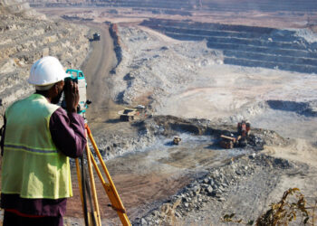 "A locally employed surveyor at an open-pit copper mine in Zambia.  He peers through his survey instrument to record the daily changes in the open-pit, and help guide mining activities to the engineer's plans."