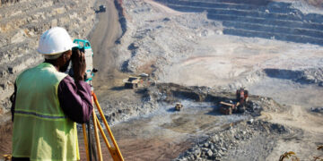 "A locally employed surveyor at an open-pit copper mine in Zambia.  He peers through his survey instrument to record the daily changes in the open-pit, and help guide mining activities to the engineer's plans."